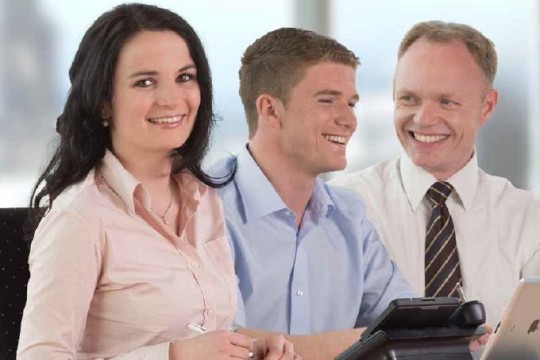 Das Bild zeigt drei Mitarbeiter im Gespräch. Die zwei Herren lachen zusammen und die Dame schaut lächelnd in die Kamera.